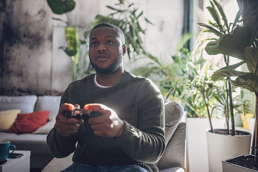 Man engrossed in video game play, holding a controller with focused intensity while gaming on his console at home.