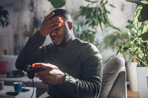 Man engrossed in video game play, holding a controller with focused intensity while gaming on his console at home.