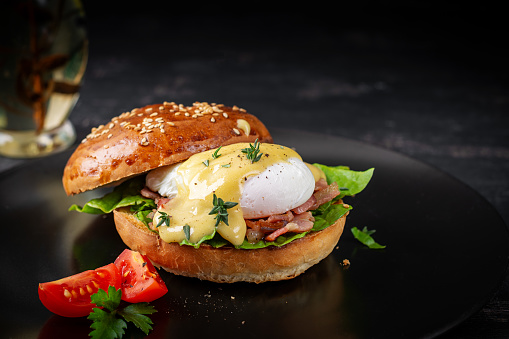 Breakfast. Sandwich with ham, poached egg, onion and arugula in a plate on a dark background