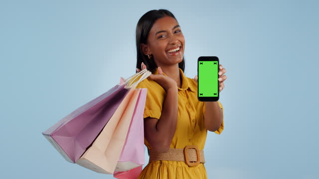 Happy woman, phone and green screen with shopping bags for advertising against a studio background. Portrait of excited female person or shopper smile showing mobile smartphone app, display or mockup