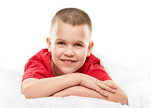 Young boy lying on his bed smiling at the camera. white background
