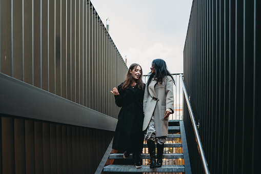 Two friends are descending a staircase in the city while they are holding their hands. They are hanging out together.