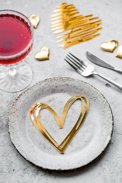 The banner. Table setting. A stylish ceramic plate, a glass of red wine, a fork and gold, red hearts on a concrete background. The concept of celebrating Valentine's Day for cafes and restaurants.
