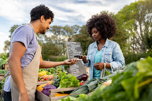 African American customer making a contactless payment at a Farmer's Market using her cell phone - small business concepts