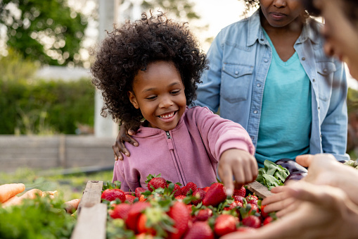 Happy African American girl buying strawberries at the Farmer's Market and smiling