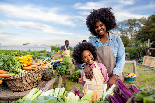 Happy African American mother and daughter selling organic vegetables at a Farmer's Market - sustainable lifestyle