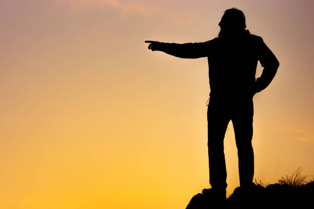 istock the silhouette of a man on an orange background points the direction with his hand 1940010189