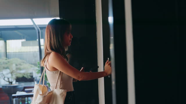 A young woman uses a fingerprint scanner to unlock a door, carrying a white tote bag