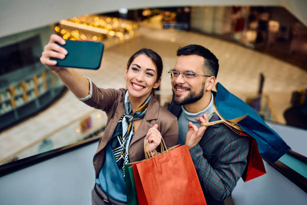 istock Young happy couple taking selfie while shopping at the mall. 1940047108