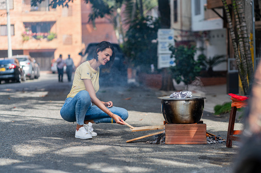 Latin woman of average age 30 years dressed comfortably is outside her house preparing a delicious wood-fired sancocho of meat and chicken that is part of Colombian culinary traditions, to share with the family