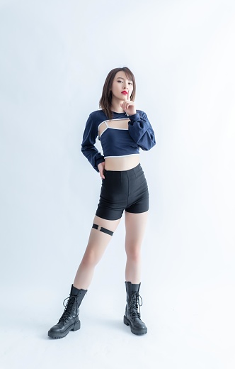 Asian woman in blue crop top and black shorts posing with finger on lips