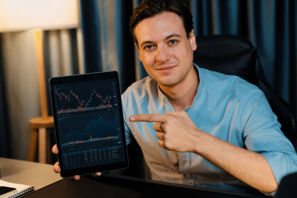 istock Trader in casual looking at camera stock with pointing laptop. Pecuniary. 1940082736