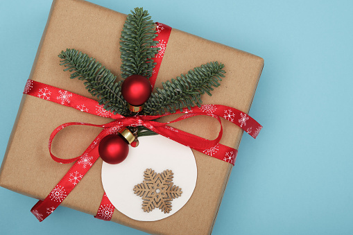 Gift box with fir tree sprig, baubles and label on light blue background