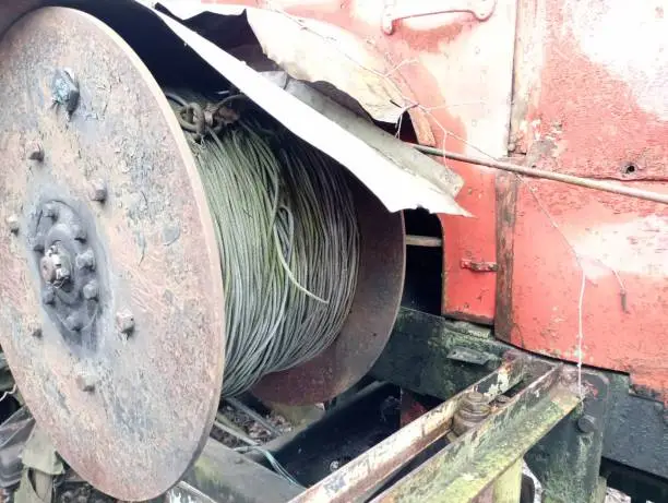 Photo of An old car long winch is wound on a special reel and mounted on an old broken machine in red.