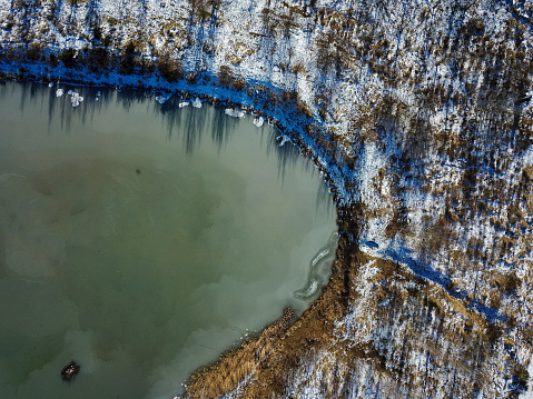 Drone view of a frozen lake with snow around it