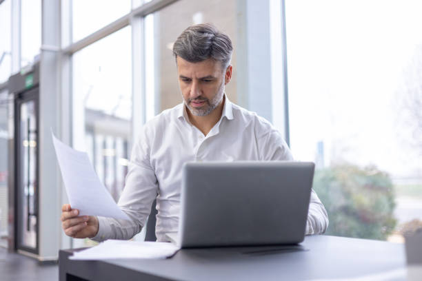 istock Man Working at Desk With Laptop and Papers in Office 1940103379
