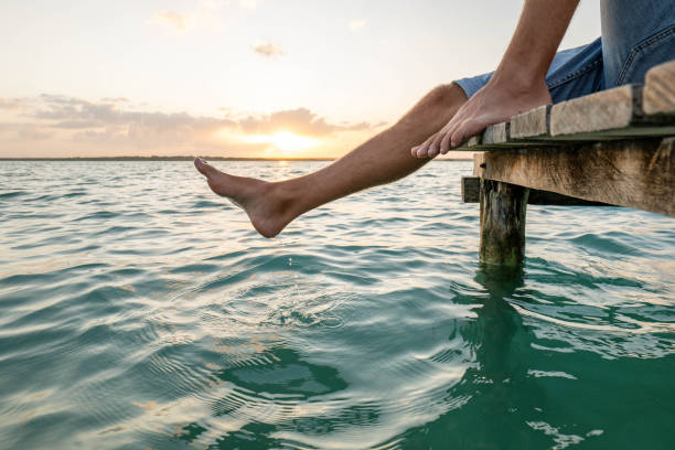 istock Man sits on pier above lake at sunrise, feet dangling 1940113700