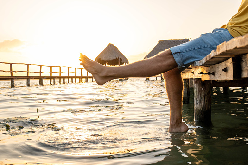 30's man on a pier above the beautiful lake of Bacalar, Mexico
Feet dangling from the wooden path.