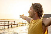 Man standing arms outstretched on a pier at sunrise