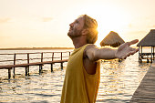 Man standing arms outstretched on a pier at sunrise