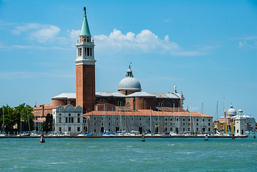 Iconic St Mark's Campanile, one of the most recognizable symbols of Venice seen against blue sky with pine trees below