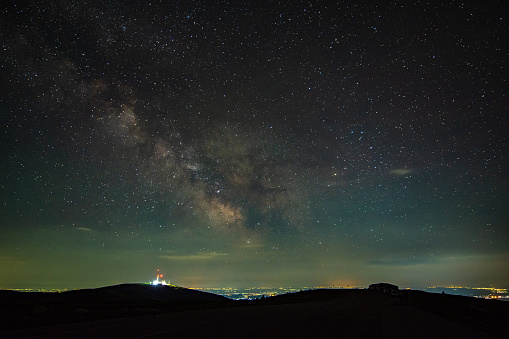 Milky way's core seen seen from the mountains, rising above a radio and gsm tower and city pollution in a summer night. Horizon is lit in orange color.