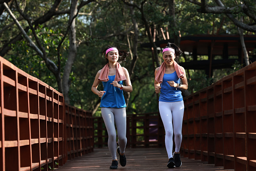 Morning jogging. Image of happy excited smiling young female, runners running together on the wooden bridge in the garden, Fitness, sports city workout concept.