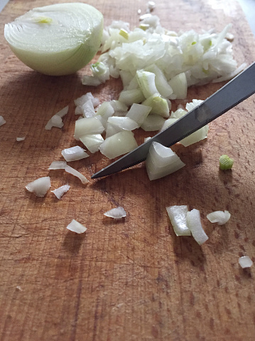 Onion cutting with kitchen knife on wooden cutting board with copy space. Cutting onion in kitchen