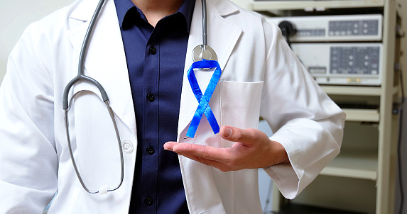 close up asian male doctor is holding blue ribbon on hands to disseminate colorectal cancer prevention and control