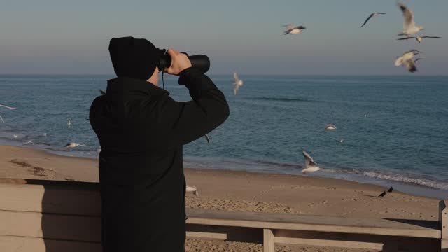 Man tourist looking through binocular standing against sea background
