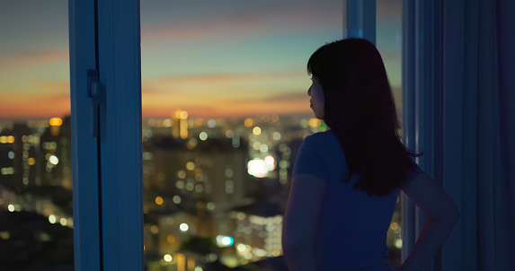 Silhouette of woman looking city at night and standing by window