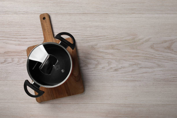 istock Black pot with glass lid on white wooden table, top view. Space for text 1940340161
