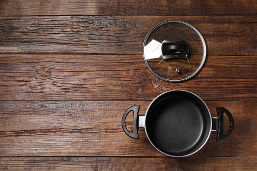 Empty black pot and glass lid on wooden table, flat lay. Space for text