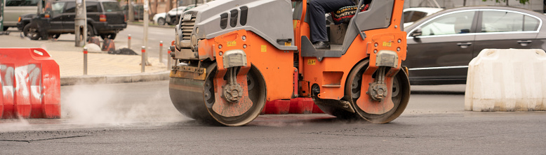 Vibratory asphalt rollers compact the new asphalt surface of the highway. Road authorities are building a new highway