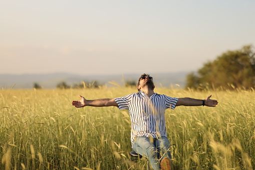 A young man in sunglasses is walking and having fun through a Sunny yellow rapeseed field, the concept of travel and freedom. summer holiday background.