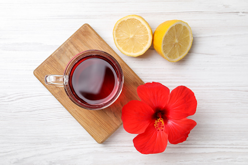 Delicious hibiscus tea, halves of lemon and beautiful flower on white wooden table, flat lay