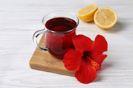 Delicious hibiscus tea, halves of lemon and beautiful flower on white wooden table