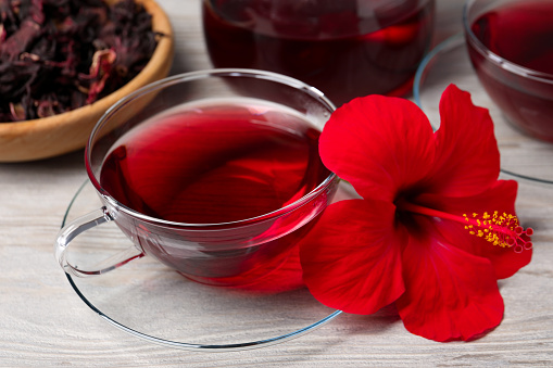Delicious hibiscus tea and beautiful flower on light wooden table, closeup