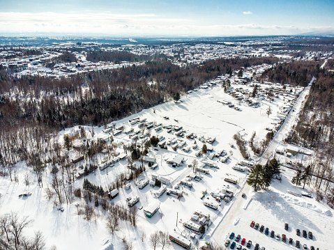 Aerial view of camping site with winterized trailers, forest, mountain and sky during winter day