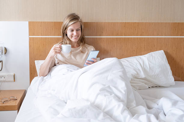istock Woman using smartphone lying in bed and drinking coffee 1940395995