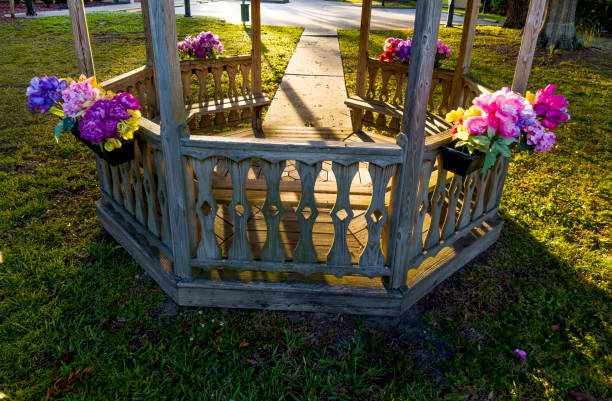 A tranquil park scene features three wooden lattice gazebos along a brick path, surrounded by lush trees and shrubs. Ideal for nature, outdoor leisure, and relaxation themes