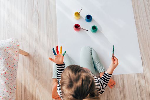 Little girl painting her hand at home.