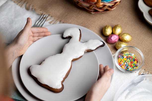 Easter bunny shaped glazed gingerbread cookie. Hands of child holding plate with biscuit