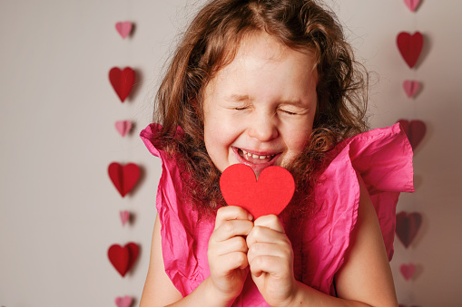 Funky little child girl in pink dress holding red heart and laughs