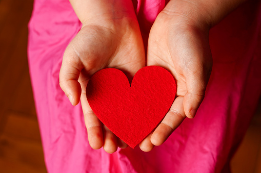 Child's hands holding bright red heart on pink background