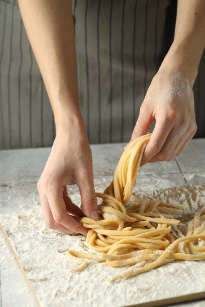 istock Woman with homemade pasta at light tiled table, closeup 1940433439