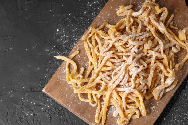 istock Board with homemade pasta and flour on dark textured table, top view. Space for text 1940434589