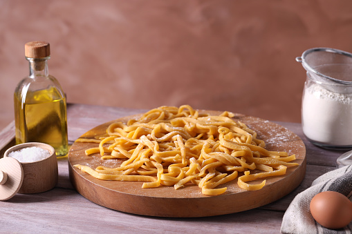 Board with homemade pasta, flour and ingredients on wooden table, space for text