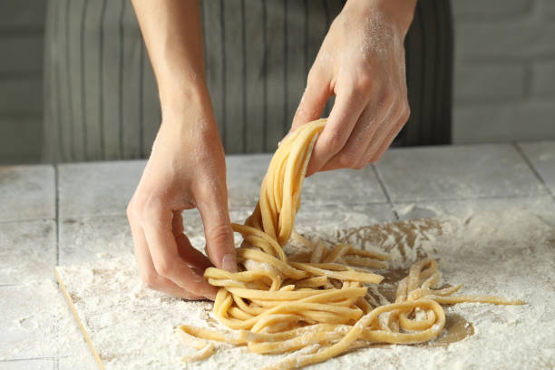 istock Woman with homemade pasta at light tiled table, closeup 1940435129