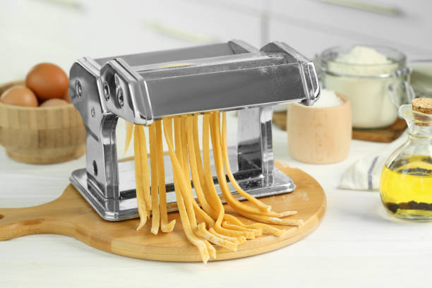 istock Pasta maker with raw dough and ingredients on white wooden table 1940436759